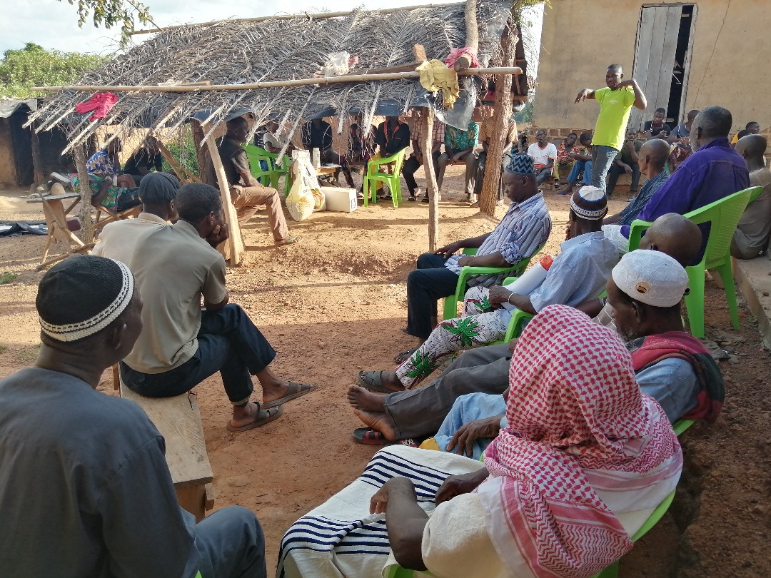 Échange avec les villageois sous un abri en chaume, dirigé par un animateur de l'entreprise AS Agri